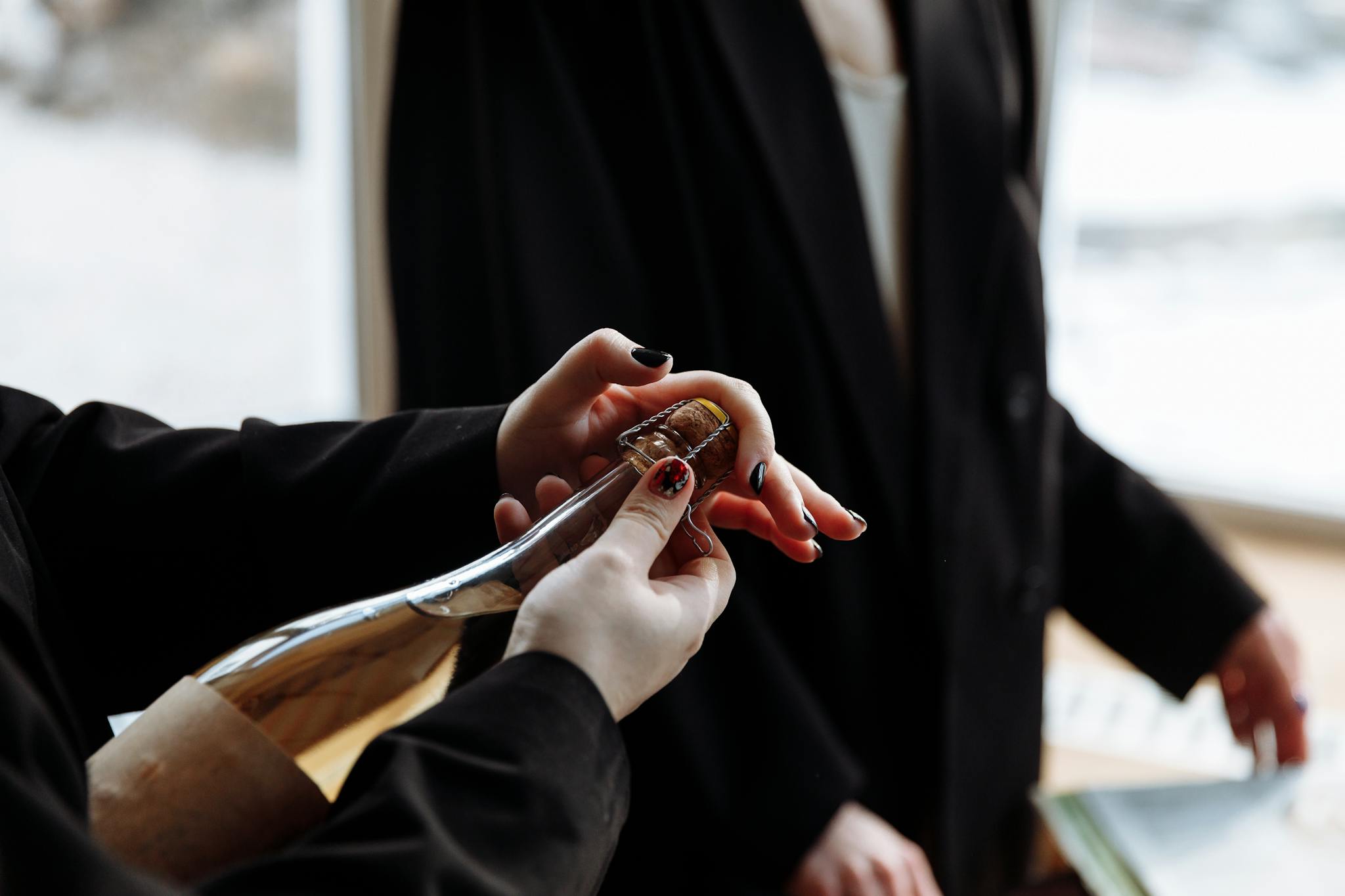 Close-up of hands opening a wine bottle in a sophisticated indoor setting.