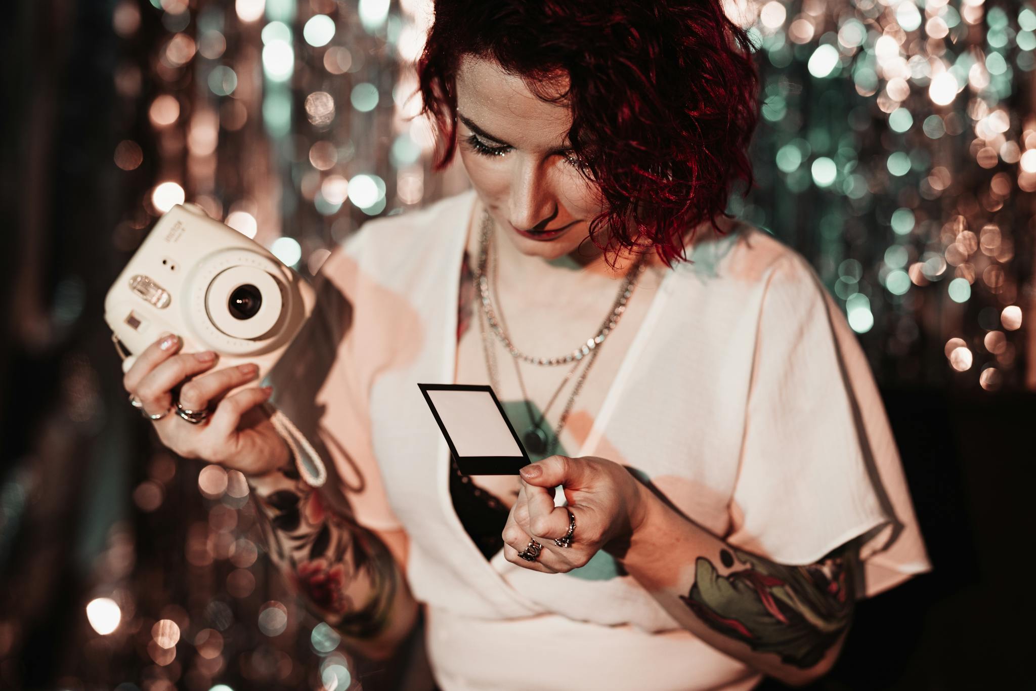 Stylish woman holding a polaroid and camera at a vibrant party with a sequin backdrop.